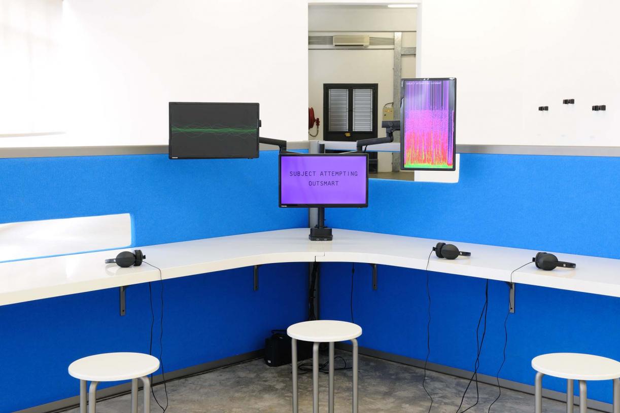 The Whole Truth, 2012, Reverse engineered lie detector, 3 channel video, stereo sound, desk, 3 chairs, 3 artificial plants, 24 minutes, 612 x 435 x 190 cm, Ed.5 + 2 AP