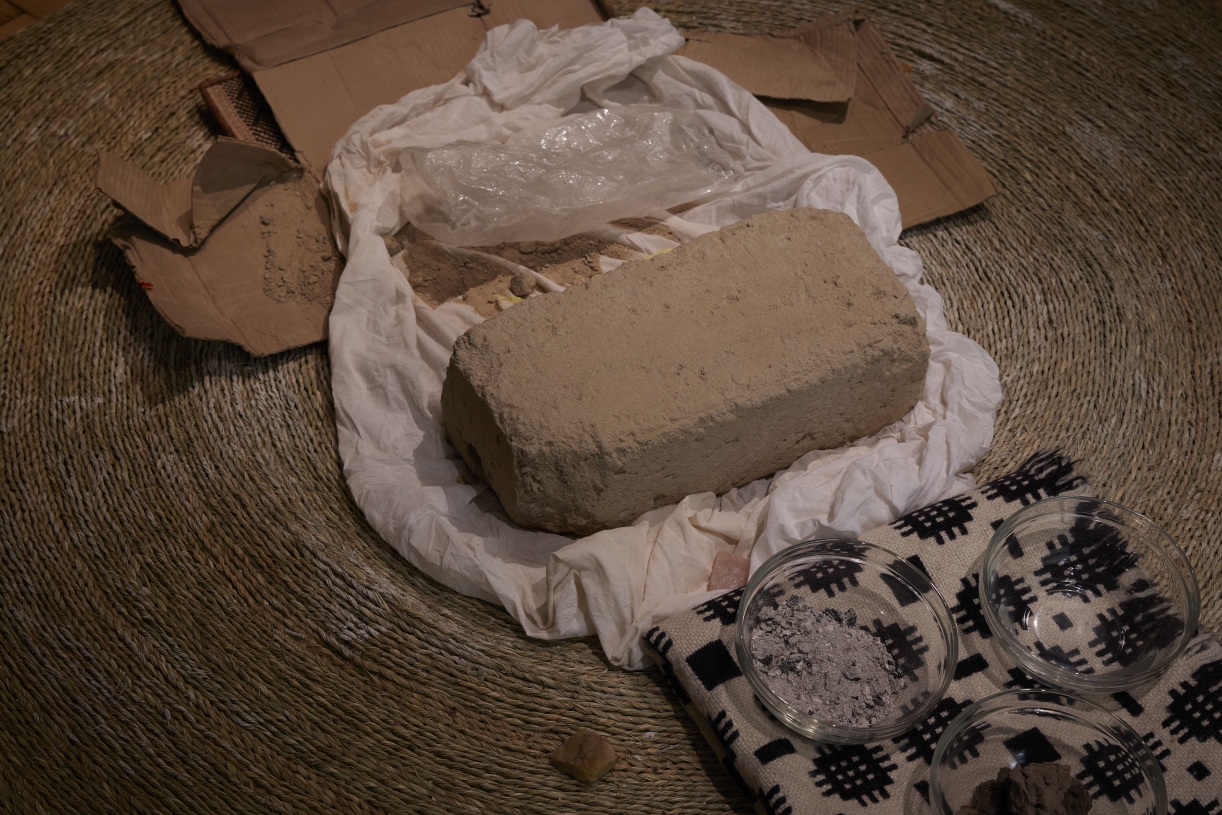 Dineo Seshee Bopape, (Nder brick) ... in process (Harmonic Conversions), 2020, Brick from Under, Senegal; woven grass mats, objects, Welsh blanket, soil from sacred site, Wales, Courtesy the bakgethwa ancestors, Installation view: Artes Mundi 9. Photography: Stuart Whipps