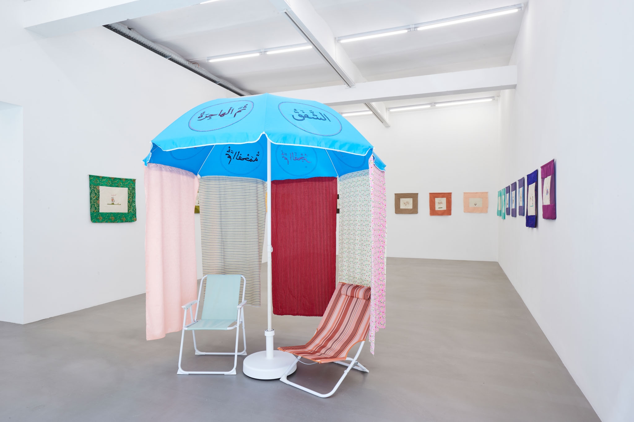 Mounira Al Solh, Aala al bahr, at the beach, 2023, Embroidered beach parasol, textile, two beach chairs, video, sound, 235 x diametre 211 cm